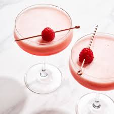 Two pink Clover Club cocktails garnished with raspberries, served in coupe glasses on a marble surface.